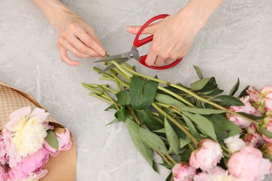 Photo of Florist making beautiful bouquet of peonies at grey marble table, top view