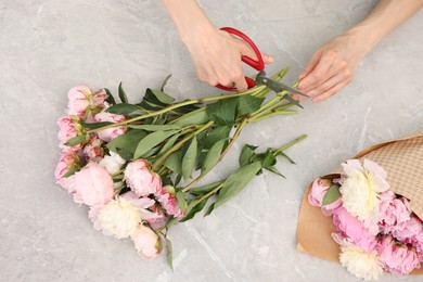 Photo of Florist making beautiful bouquet of peonies at grey marble table, top view