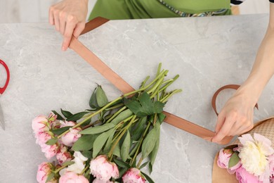 Photo of Florist making beautiful bouquet of peonies at grey marble table, top view