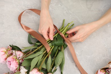 Photo of Florist making beautiful bouquet of peonies at grey marble table, top view