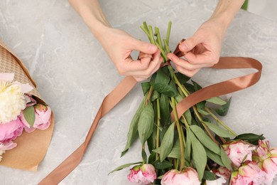 Photo of Florist making beautiful bouquet of peonies at grey marble table, top view