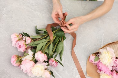 Photo of Florist making beautiful bouquet of peonies at grey marble table, top view