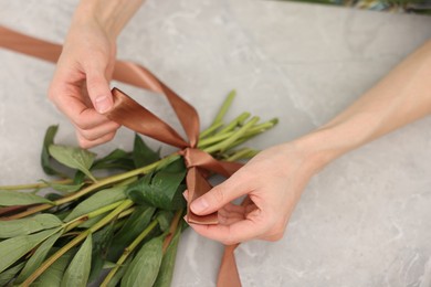 Photo of Florist making beautiful bouquet of flowers at grey marble table, top view