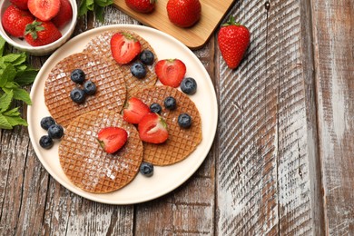 Photo of Tasty Dutch waffles (stroopwafels), mint and berries on wooden table, flat lay. Space for text