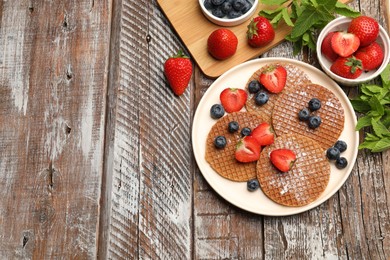 Photo of Tasty Dutch waffles (stroopwafels), mint and berries on wooden table, flat lay. Space for text
