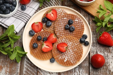 Photo of Tasty Dutch waffles (stroopwafels), mint and berries on wooden table, flat lay