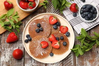 Photo of Tasty Dutch waffles (stroopwafels), mint and berries on wooden table, flat lay