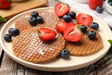 Photo of Tasty Dutch waffles (stroopwafels) and berries on wooden table, closeup