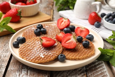 Photo of Tasty Dutch waffles (stroopwafels), mint and berries on wooden table, closeup