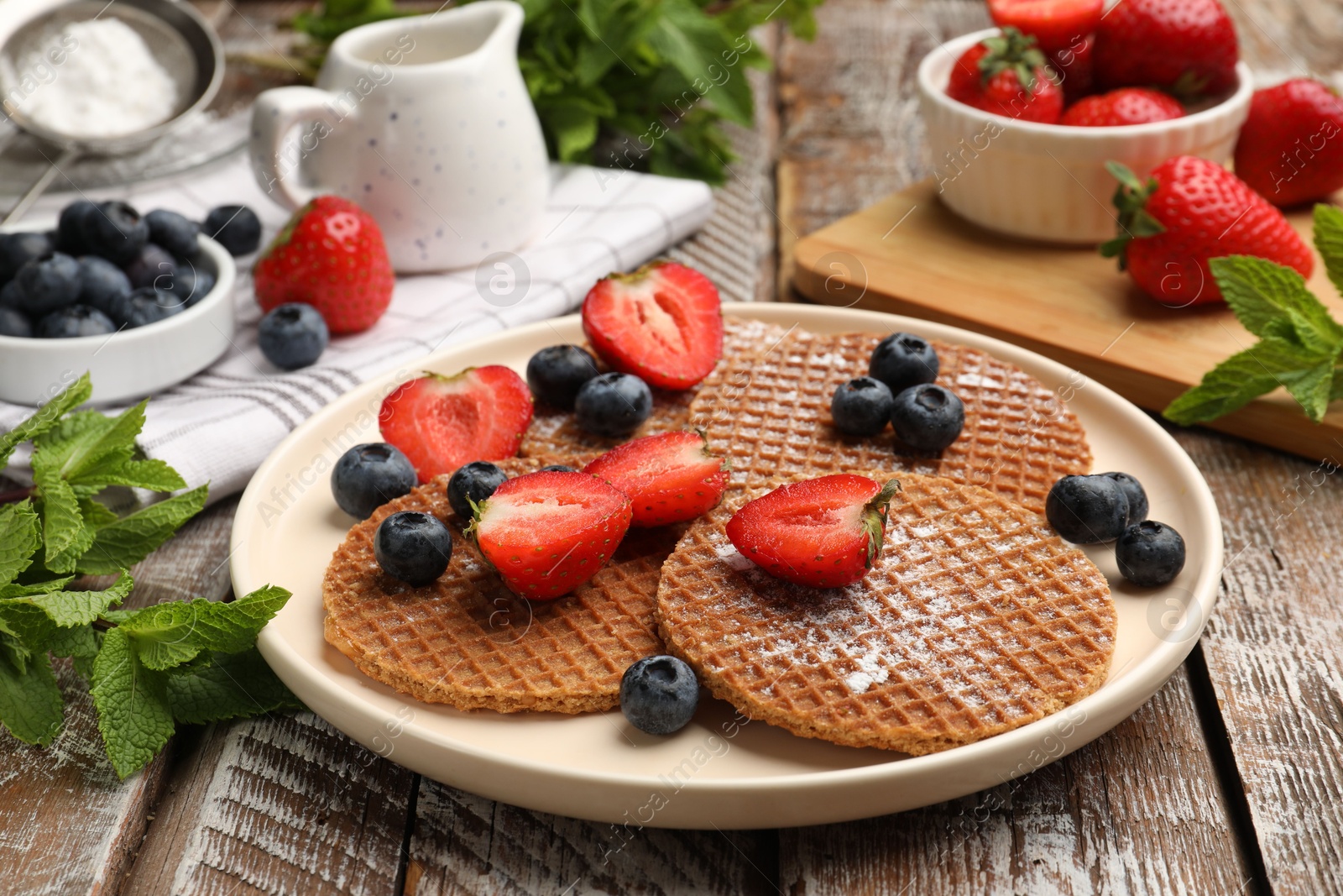 Tasty Dutch waffles (stroopwafels), mint and berries on wooden table, closeup Photo of Tasty Dutch waffles (stroopwafels), mint and berries on wooden table, closeup