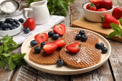 Photo of Tasty Dutch waffles (stroopwafels), mint and berries on wooden table, closeup