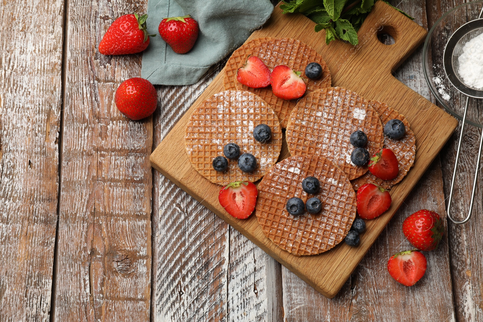 Tasty Dutch waffles (stroopwafels), mint and berries on wooden table, flat lay. Space for text Photo of Tasty Dutch waffles (stroopwafels), mint and berries on wooden table, flat lay. Space for text