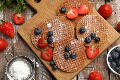 Photo of Tasty Dutch waffles (stroopwafels), mint and berries on wooden table, flat lay