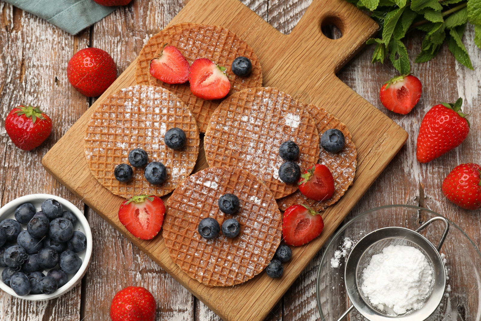 Tasty Dutch waffles (stroopwafels), mint and berries on wooden table, flat lay Photo of Tasty Dutch waffles (stroopwafels), mint and berries on wooden table, flat lay