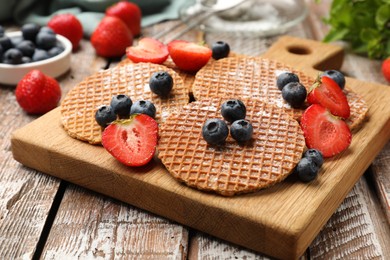 Photo of Tasty Dutch waffles (stroopwafels) and berries on wooden table, closeup
