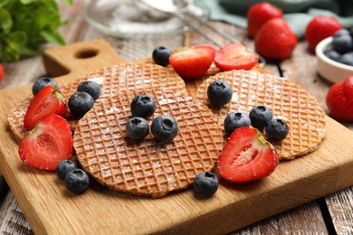 Photo of Tasty Dutch waffles (stroopwafels) and berries on wooden table, closeup
