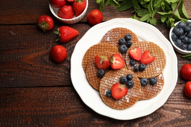 Photo of Tasty Dutch waffles (stroopwafels), mint and berries on wooden table, flat lay. Space for text