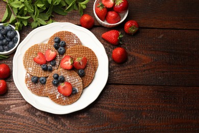 Photo of Tasty Dutch waffles (stroopwafels), mint and berries on wooden table, flat lay. Space for text