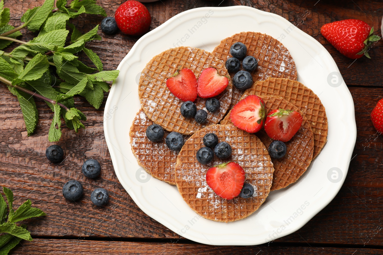 Tasty Dutch waffles (stroopwafels), mint and berries on wooden table, flat lay Photo of Tasty Dutch waffles (stroopwafels), mint and berries on wooden table, flat lay