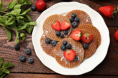 Photo of Tasty Dutch waffles (stroopwafels), mint and berries on wooden table, flat lay