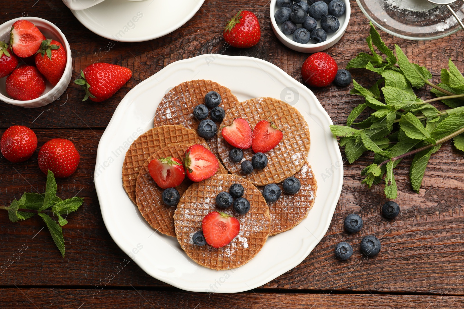 Tasty Dutch waffles (stroopwafels), mint and berries on wooden table, flat lay Photo of Tasty Dutch waffles (stroopwafels), mint and berries on wooden table, flat lay