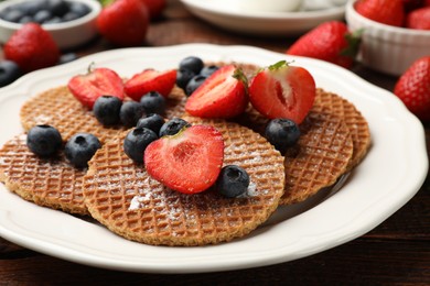 Photo of Tasty Dutch waffles (stroopwafels) and berries on wooden table, closeup