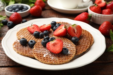 Photo of Tasty Dutch waffles (stroopwafels) and berries on wooden table, closeup