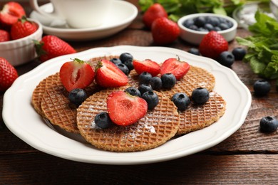 Photo of Tasty Dutch waffles (stroopwafels) and berries on wooden table, closeup