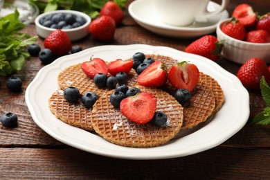 Photo of Tasty Dutch waffles (stroopwafels) and berries on wooden table, closeup