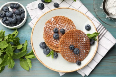 Photo of Tasty Dutch waffles (stroopwafels), mint and blueberries on light blue wooden table, flat lay