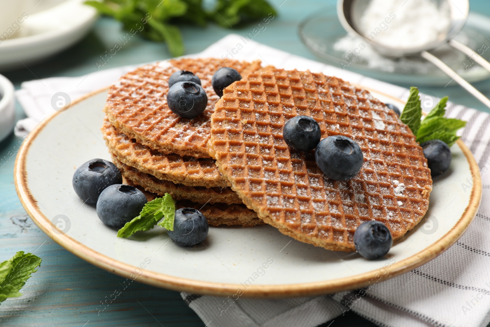 Tasty Dutch waffles (stroopwafels), mint and blueberries on light blue wooden table, closeup Photo of Tasty Dutch waffles (stroopwafels), mint and blueberries on light blue wooden table, closeup
