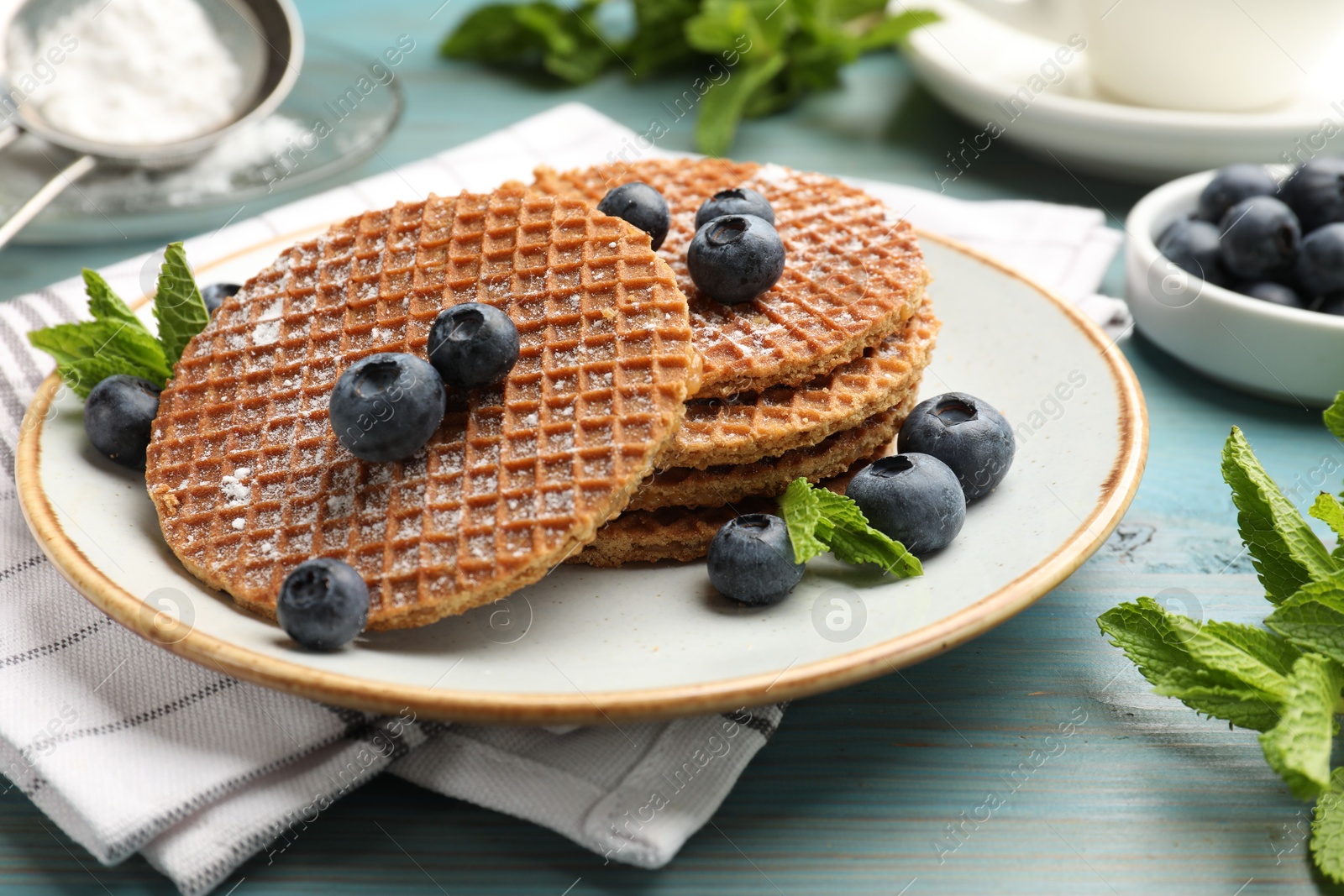 Tasty Dutch waffles (stroopwafels), mint and blueberries on light blue wooden table, closeup Photo of Tasty Dutch waffles (stroopwafels), mint and blueberries on light blue wooden table, closeup