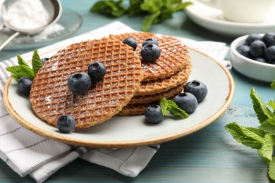 Photo of Tasty Dutch waffles (stroopwafels), mint and blueberries on light blue wooden table, closeup