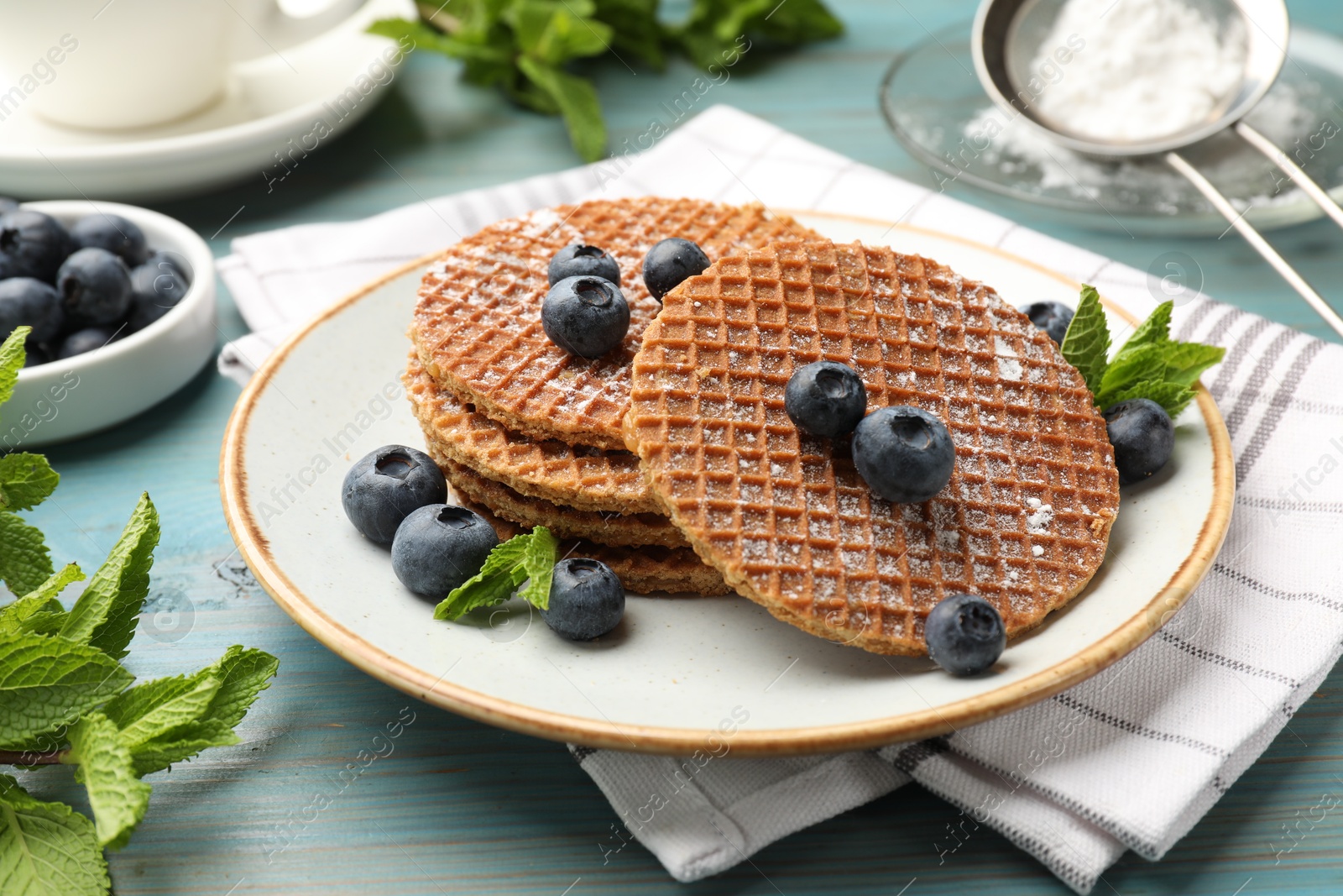 Tasty Dutch waffles (stroopwafels), mint and blueberries on light blue wooden table, closeup Photo of Tasty Dutch waffles (stroopwafels), mint and blueberries on light blue wooden table, closeup