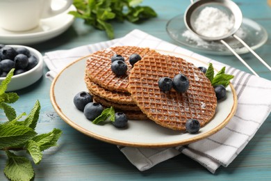 Photo of Tasty Dutch waffles (stroopwafels), mint and blueberries on light blue wooden table, closeup