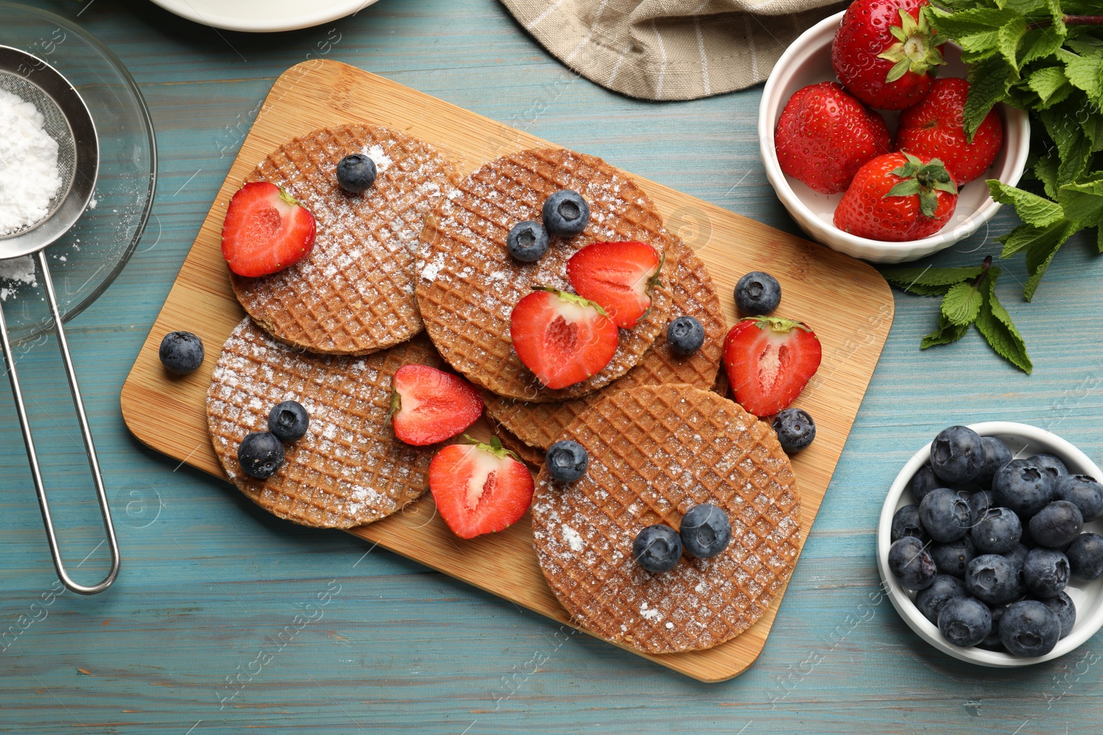 Tasty Dutch waffles (stroopwafels), mint and berries on light blue wooden table, flat lay Photo of Tasty Dutch waffles (stroopwafels), mint and berries on light blue wooden table, flat lay