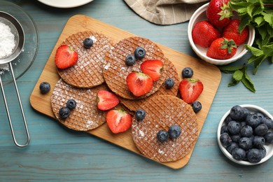 Photo of Tasty Dutch waffles (stroopwafels), mint and berries on light blue wooden table, flat lay