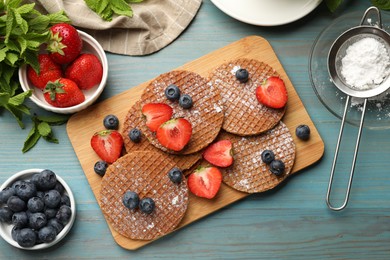 Photo of Tasty Dutch waffles (stroopwafels), mint and berries on light blue wooden table, flat lay