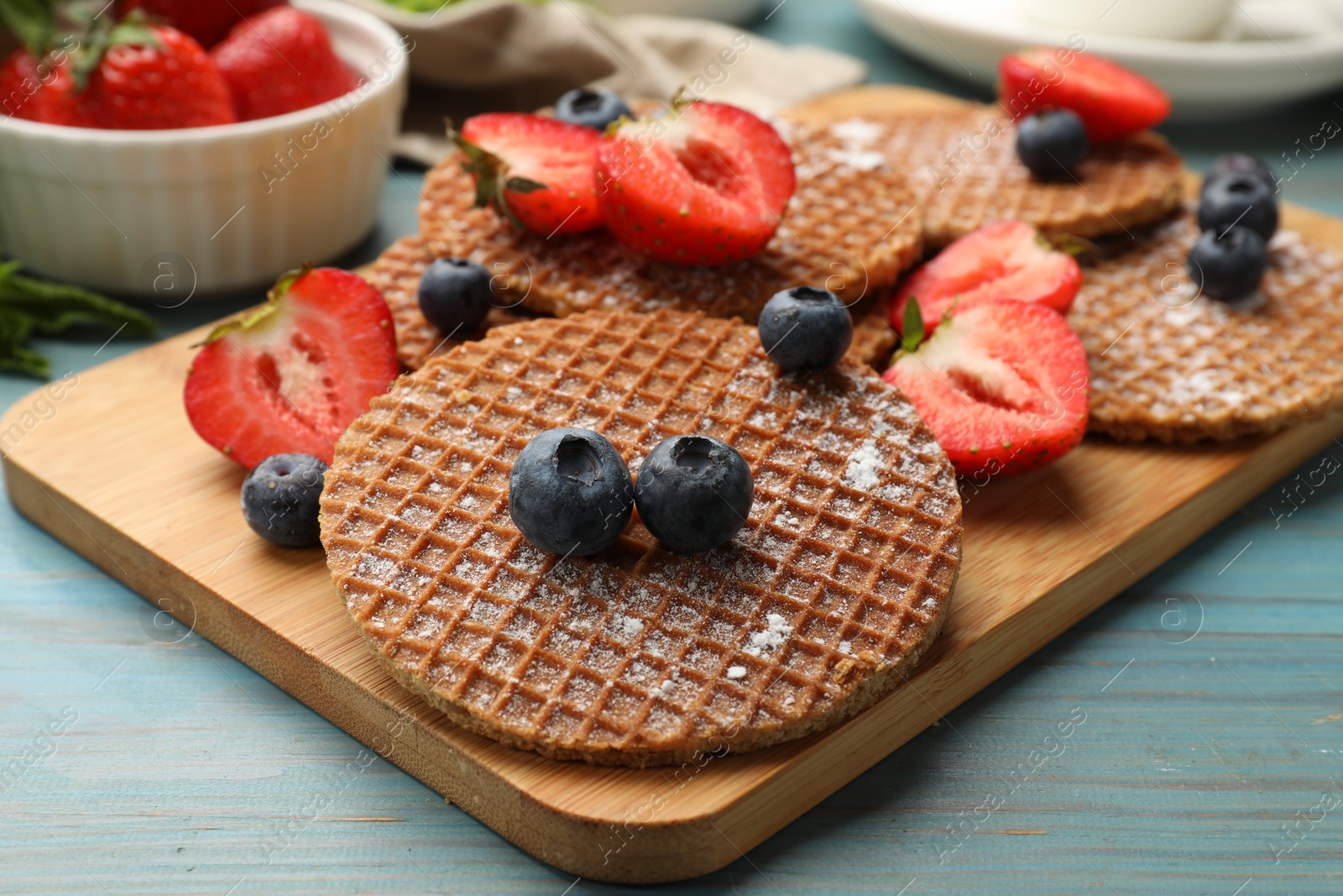 Tasty Dutch waffles (stroopwafels) and berries on light blue wooden table, closeup Photo of Tasty Dutch waffles (stroopwafels) and berries on light blue wooden table, closeup