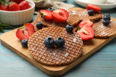 Photo of Tasty Dutch waffles (stroopwafels) and berries on light blue wooden table, closeup