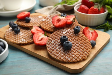 Photo of Tasty Dutch waffles (stroopwafels) and berries on light blue wooden table, closeup