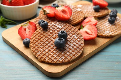 Photo of Tasty Dutch waffles (stroopwafels) and berries on light blue wooden table, closeup