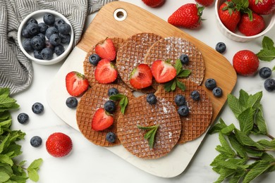Photo of Tasty Dutch waffles (stroopwafels), mint and berries on white marble table, flat lay