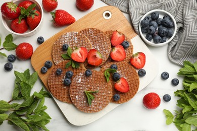 Photo of Tasty Dutch waffles (stroopwafels), mint and berries on white marble table, flat lay
