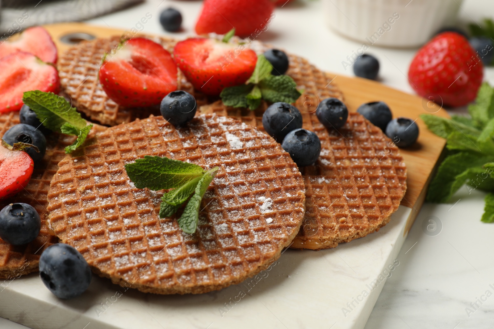 Tasty Dutch waffles (stroopwafels), mint and strawberries on white marble table, closeup Photo of Tasty Dutch waffles (stroopwafels), mint and strawberries on white marble table, closeup