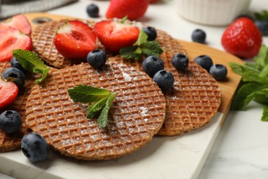 Photo of Tasty Dutch waffles (stroopwafels), mint and strawberries on white marble table, closeup