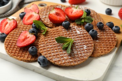 Photo of Tasty Dutch waffles (stroopwafels), mint and strawberries on white marble table, closeup