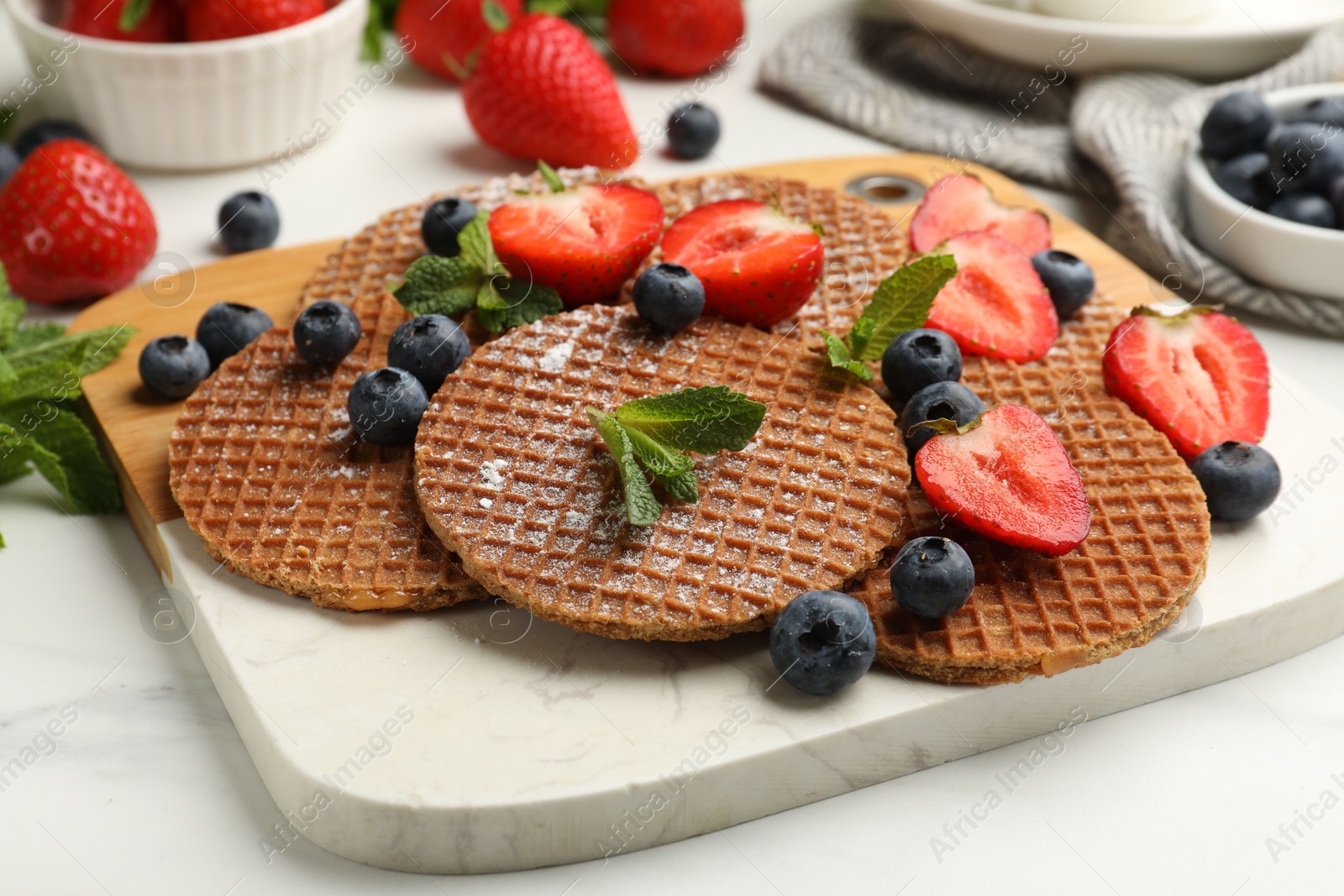 Tasty Dutch waffles (stroopwafels), mint and strawberries on white marble table, closeup Photo of Tasty Dutch waffles (stroopwafels), mint and strawberries on white marble table, closeup