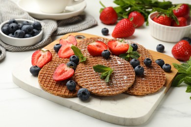 Photo of Tasty Dutch waffles (stroopwafels), mint and strawberries on white marble table, closeup