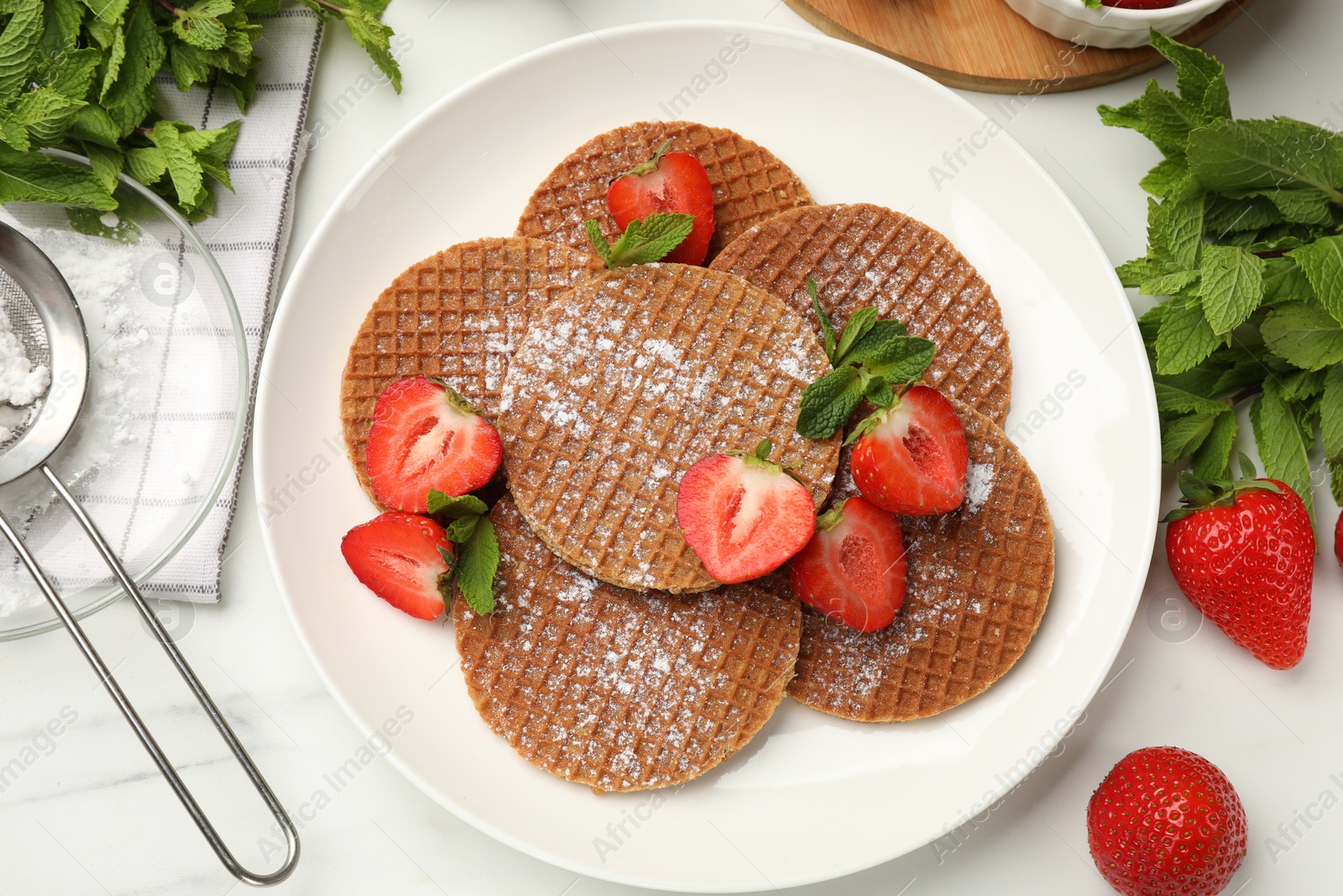 Tasty Dutch waffles (stroopwafels), mint and strawberries on white marble table, flat lay Photo of Tasty Dutch waffles (stroopwafels), mint and strawberries on white marble table, flat lay
